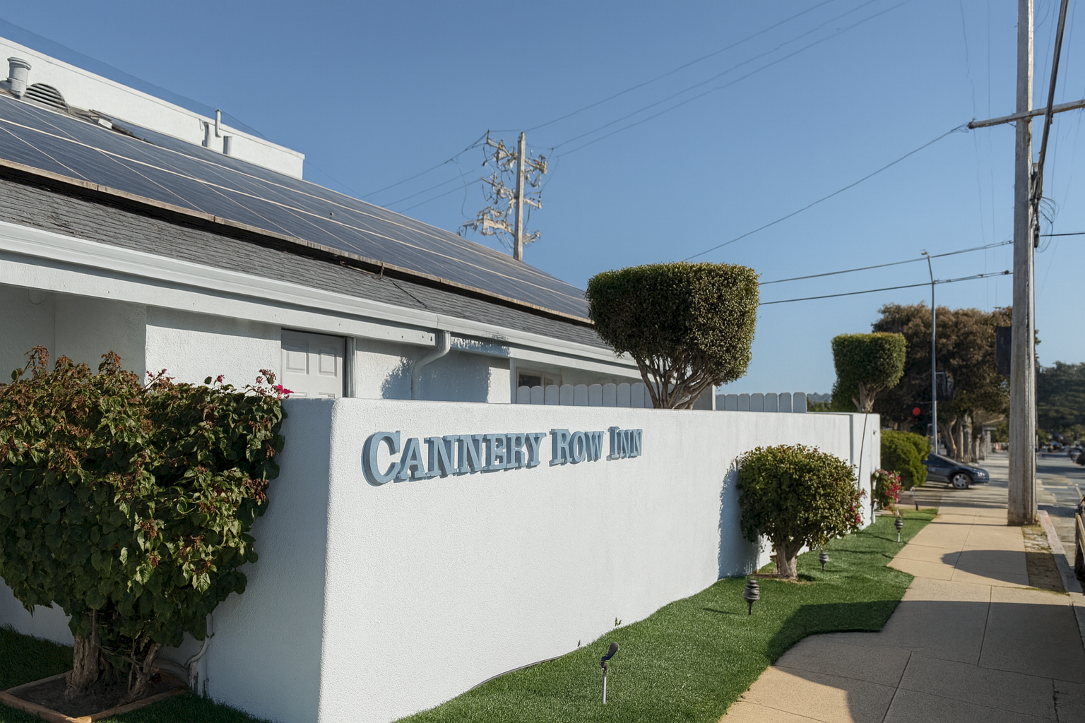 Cannery Row Inn is the sign on a light-colored wall along a sunny sidewalk.