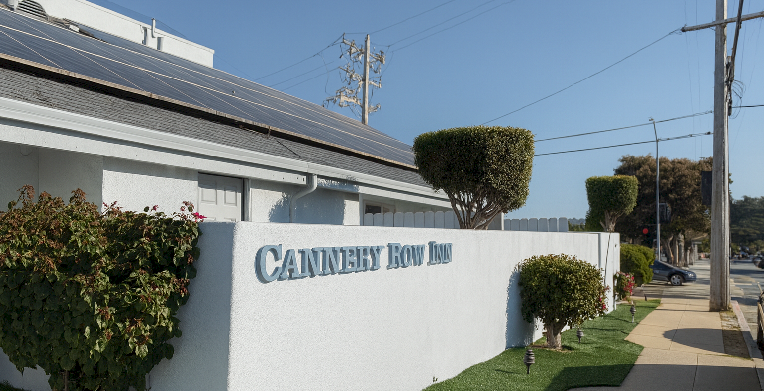 Cannery Row Inn is the sign on a light-colored wall along a sunny sidewalk.