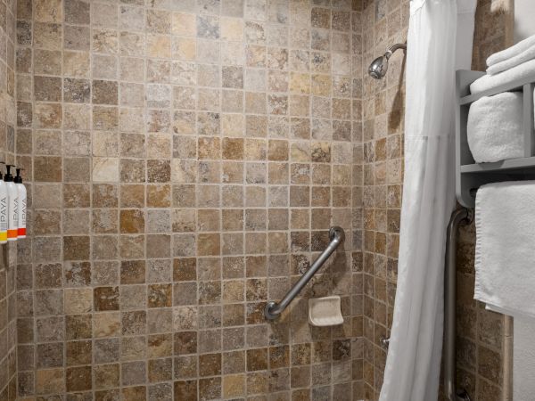 A tiled shower with a grab bar, a mounted shampoo set on the wall, a shower curtain, and a stacked towel shelf on the right. ending here