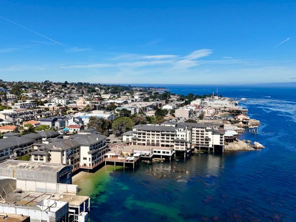 Coastal town with cluster of houses along rocky shoreline, docks and colorful buildings by clear blue water under a bright sky.