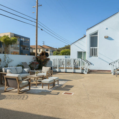 Cutur street scene with outdoor cafe tables and chairs on a sunny day, modern buildings, parked scooter, and pedestrians stroll by.
