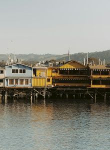 Colorful houses perched along a calm waterway, with boats docked and hills in the background.