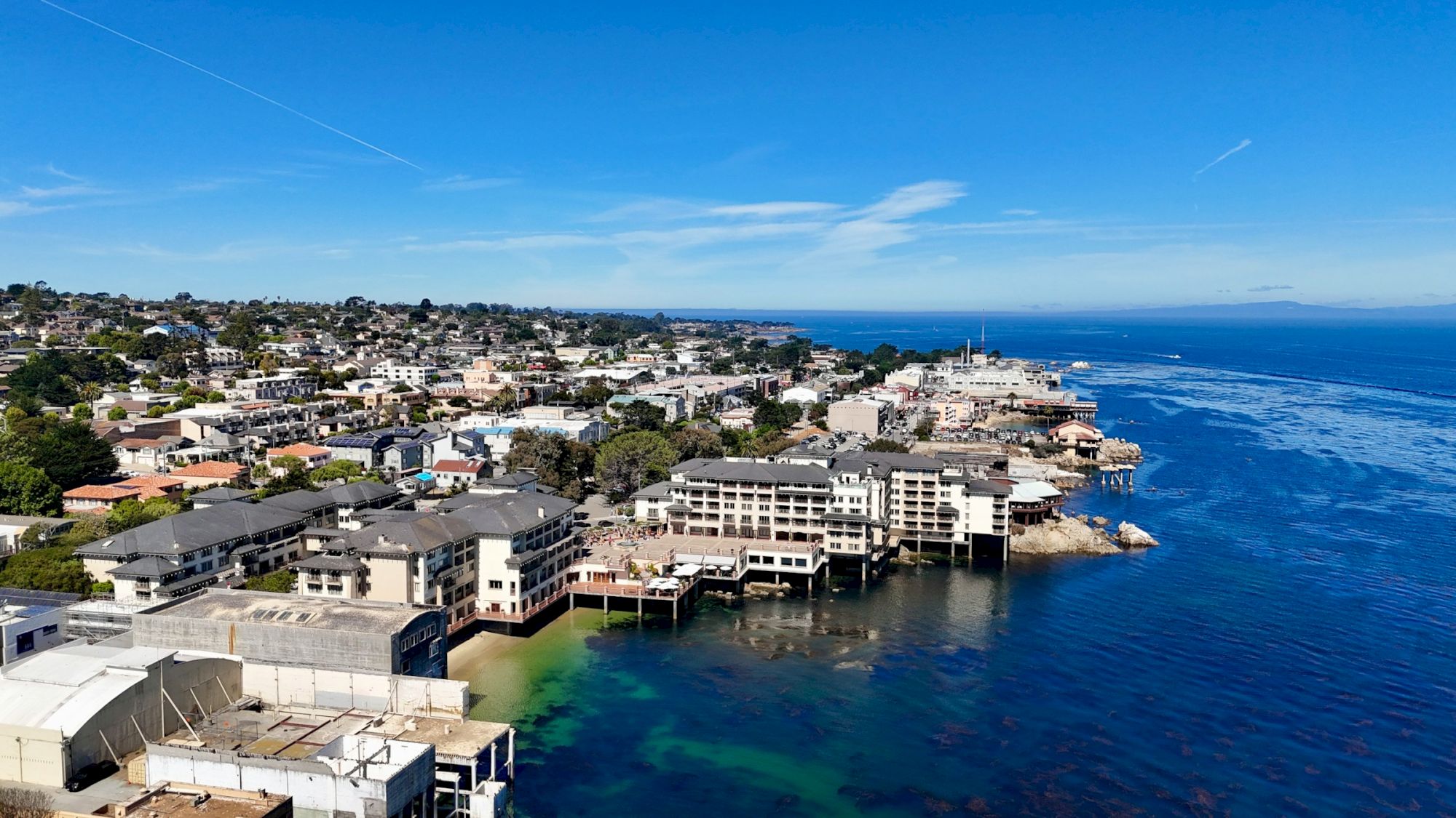 Beachfront houses along a rocky coastline with blue ocean, clear sky, and calm water&mdash;coastal neighborhood seen from above.