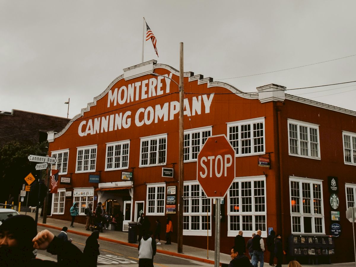 A bright red brick building labeled Monterey Canning Company sits at a street corner with a stop sign and power lines overhead.