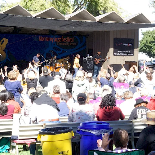 Live jazz band performing at the Monterey Jazz Festival stage with crowd cheering in front of a big banner.